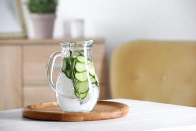 Refreshing cucumber water with rosemary in jug on white table. Space for text