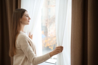 Photo of Woman opening elegant window curtains in room