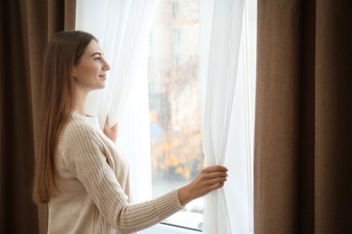 Woman opening elegant window curtains in room