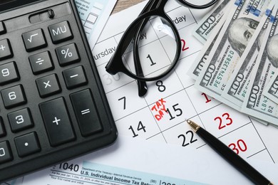 Photo of Calendar with date reminder about tax day, documents, money, pen, calculator and glasses on table, top view