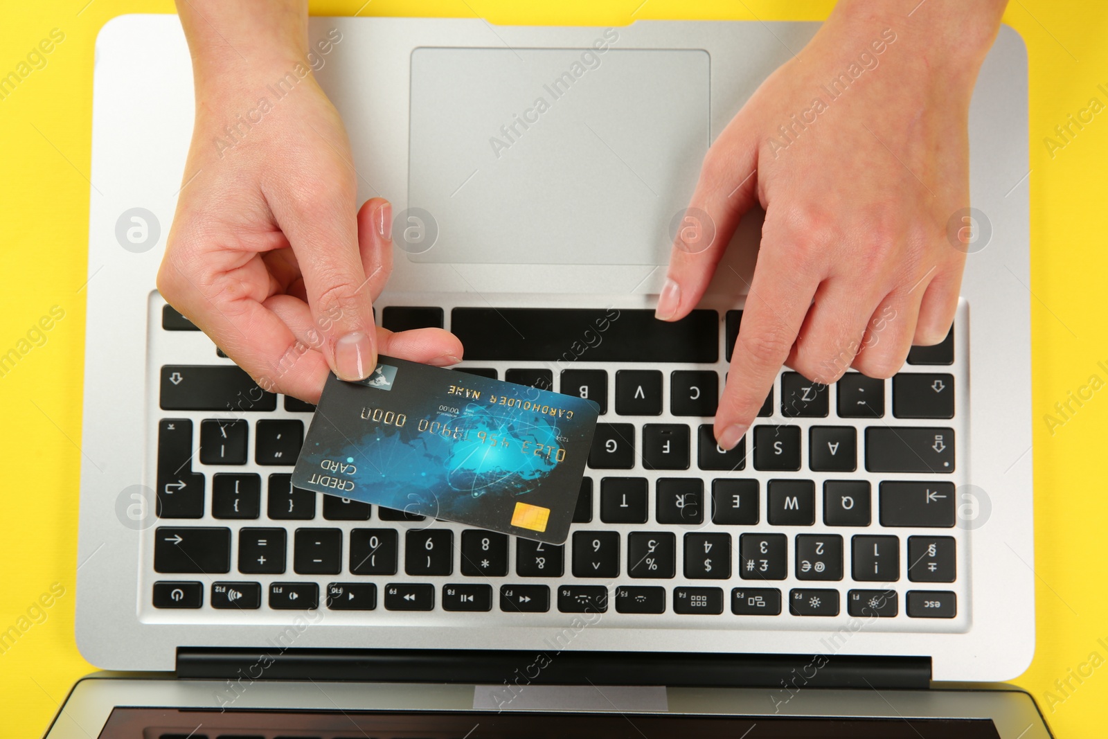 Photo of Online payment. Woman using credit card and laptop at yellow table, top view