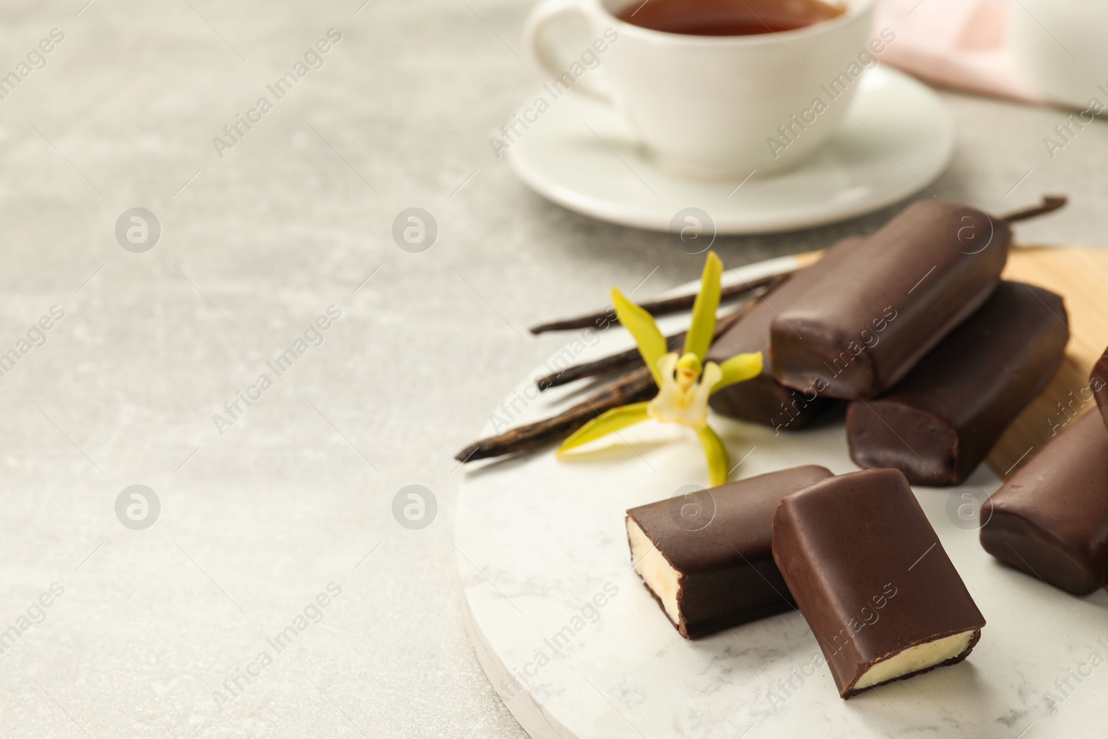 Photo of Glazed curd cheese bars, vanilla pods and flower on grey table, closeup. Space for text