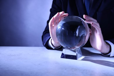 Businessman using crystal ball to predict future at table, closeup. Space for text