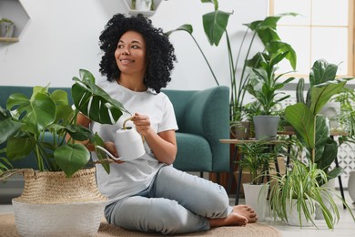 Photo of Happy woman watering beautiful monstera with water at home. Houseplant care