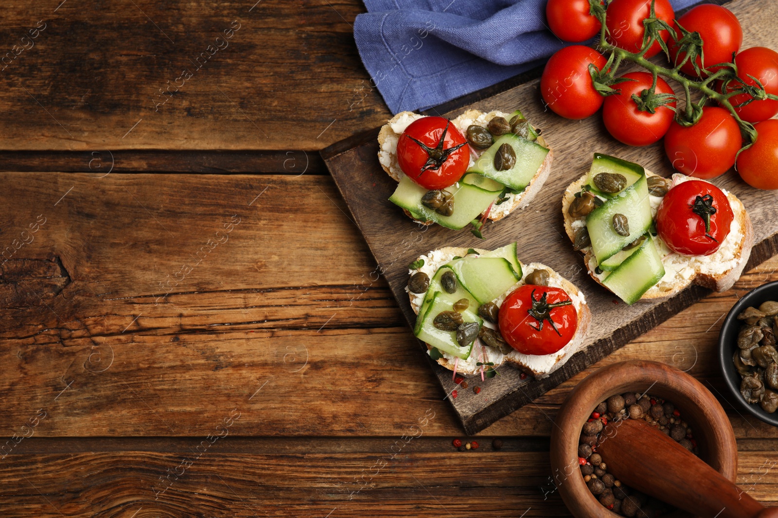 Photo of Bruschettas with capers, vegetables and cream cheese served on wooden table, flat lay. Space for text