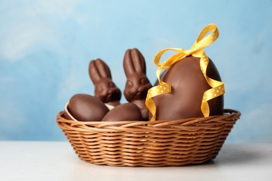 Photo of Wicker basket with sweet chocolate Easter eggs and bunnies on table against color background