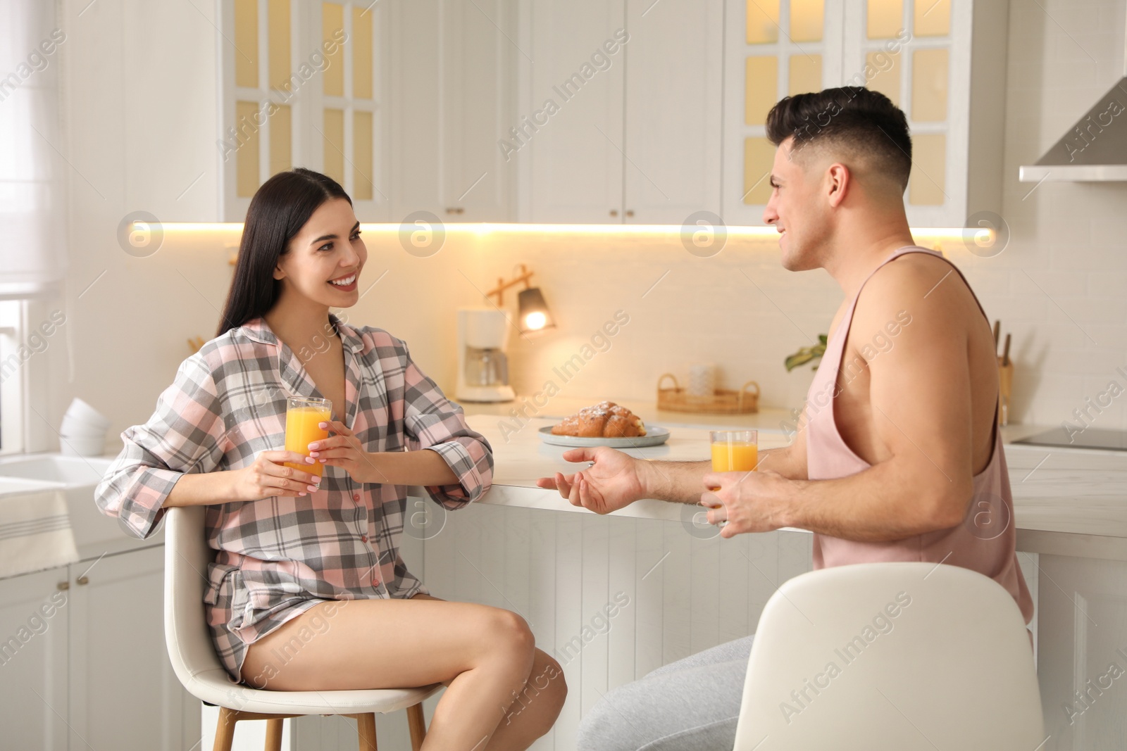 Photo of Happy couple wearing pyjamas during breakfast at table in kitchen