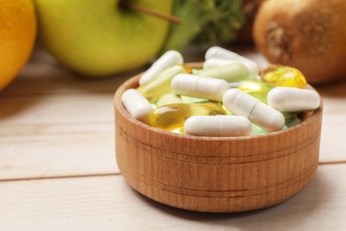 Photo of Dietary supplements. Bowl with different pills near food products on light wooden table, closeup. Space for text