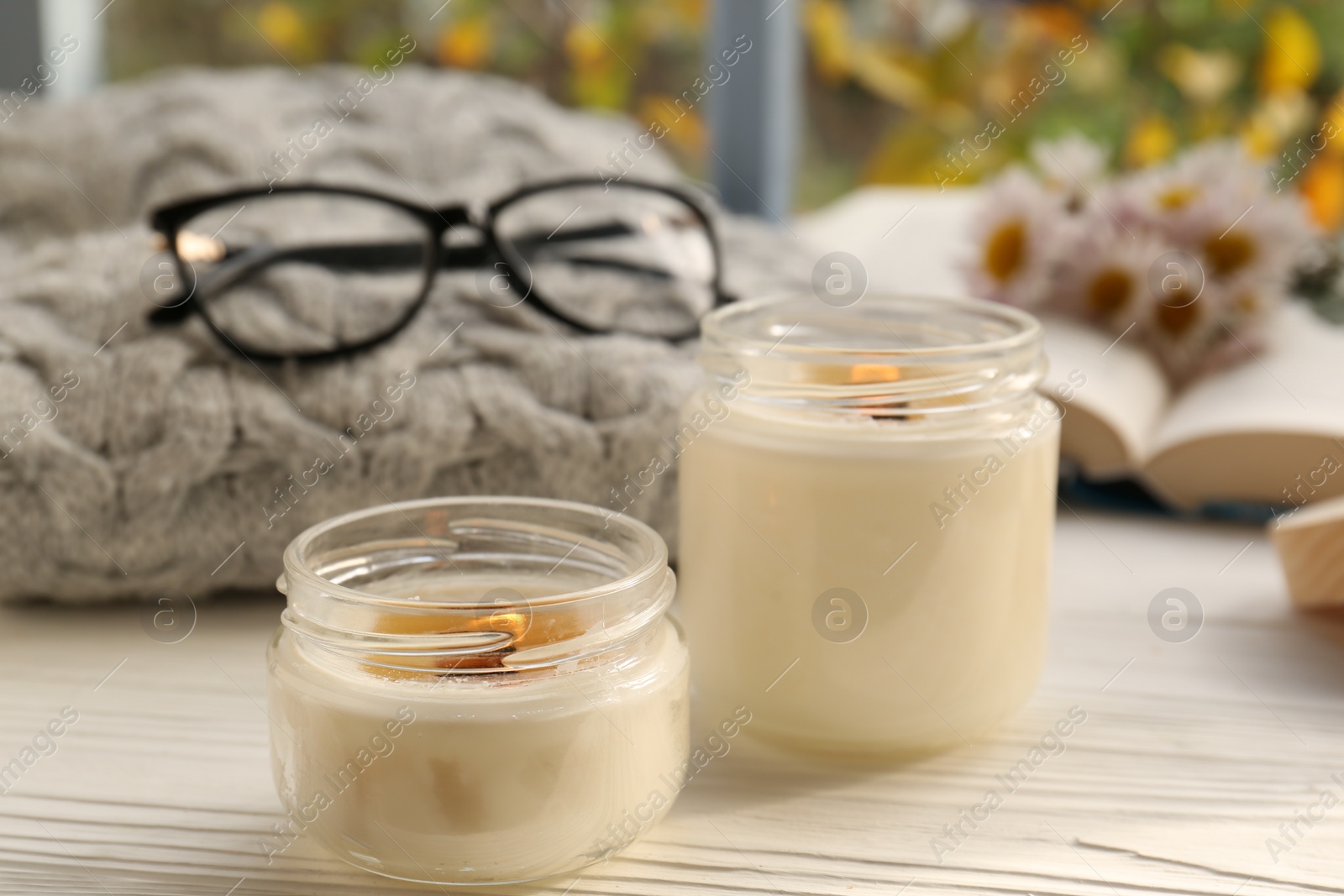 Photo of Burning scented candles, warm sweater, glasses and chamomile flowers on white wooden table near window