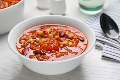 Bowl with tasty chili con carne on white wooden table, closeup