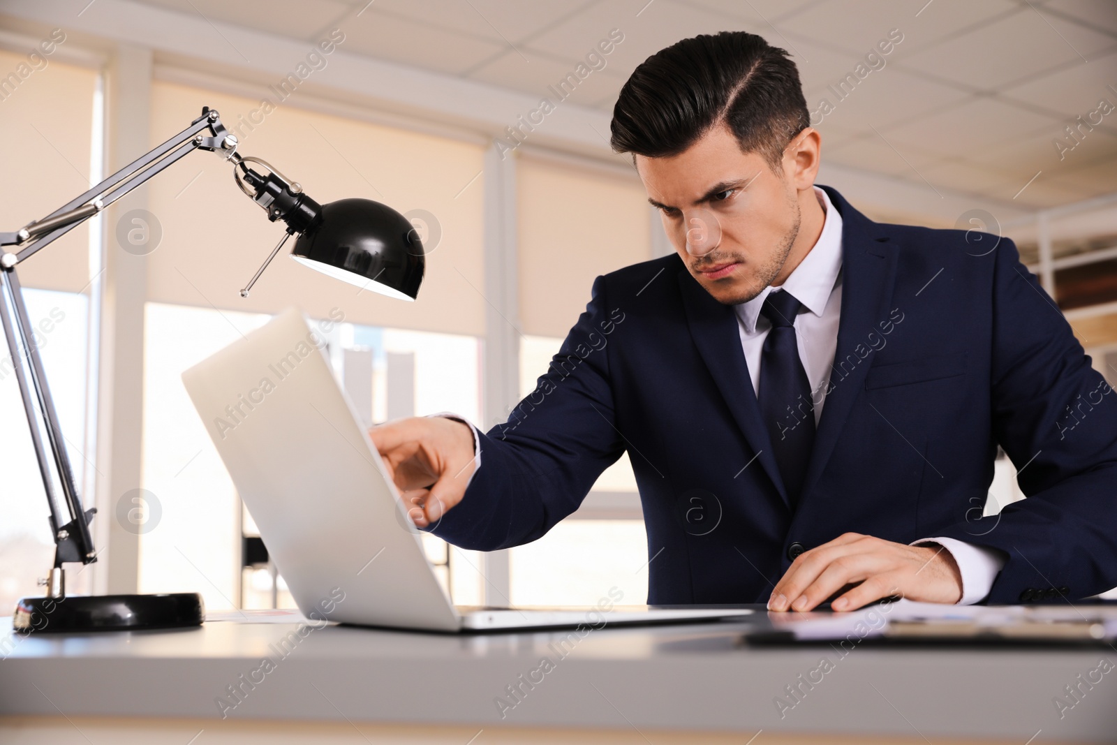 Photo of Emotional businessman with laptop at table in office