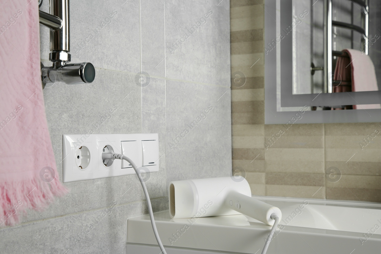 Photo of Hairdryer plugged into power socket on light grey wall in bathroom, space for text