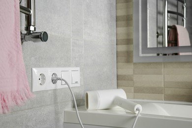 Hairdryer plugged into power socket on light grey wall in bathroom, space for text