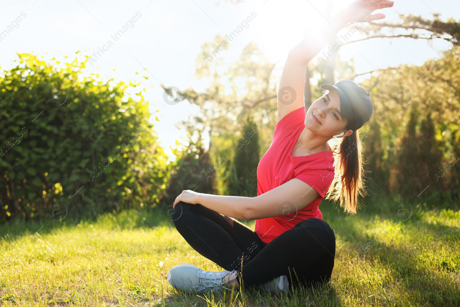 Photo of Young woman listening to music while doing morning exercise on green grass in park, space for text