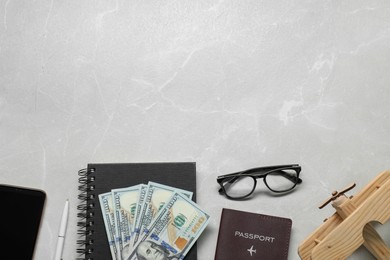 Flat lay composition with dollars, passport and wooden model of plane on light marble table, space for text. Business trip