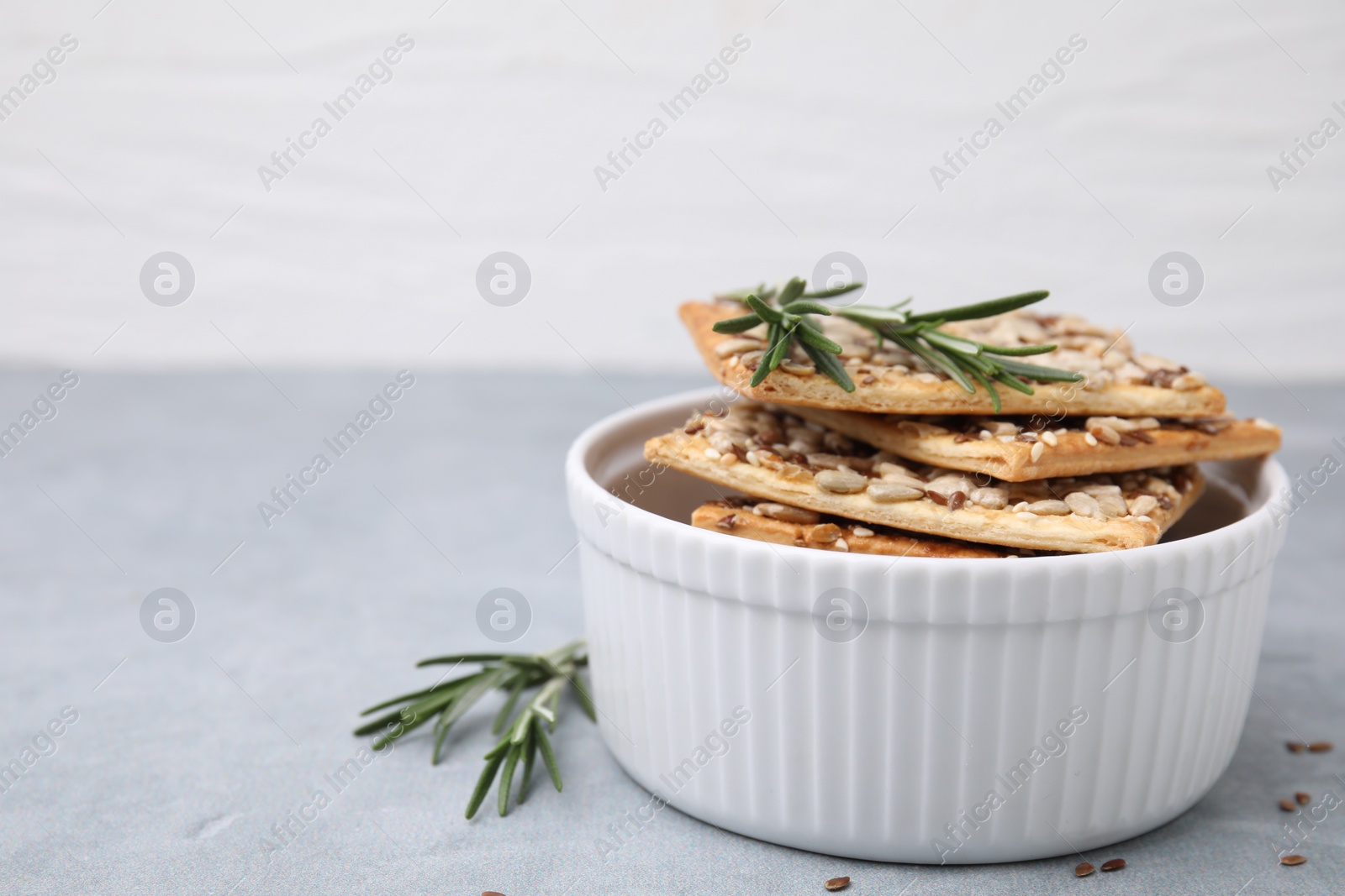 Photo of Cereal crackers with flax, sunflower, sesame seeds and rosemary in bowl on grey table, closeup. Space for text