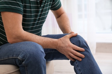 Photo of Senior man suffering from knee pain at home, closeup