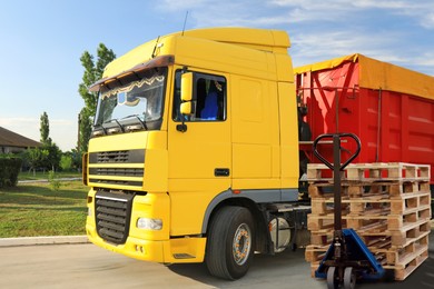 Image of Modern manual forklift with wooden pallets near trucks outdoors on sunny day