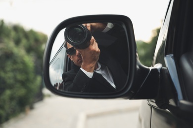 Private detective with camera spying from auto, view through car side mirror