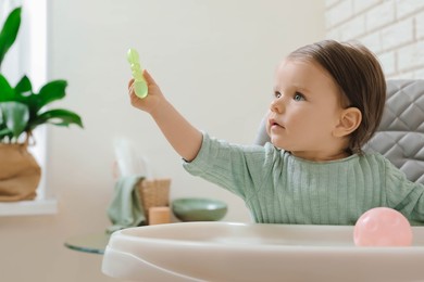 Cute little baby with teether in high chair indoors