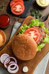 Delicious burger with beef patty and ingredients on wooden table, flat lay