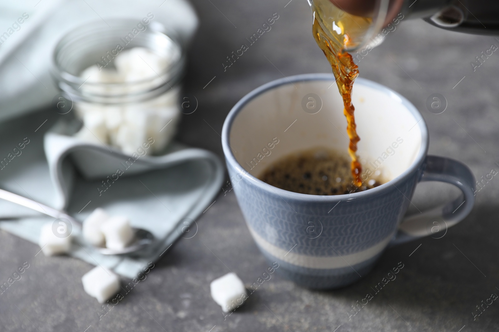 Photo of Pouring hot coffee into cup on grey table, closeup