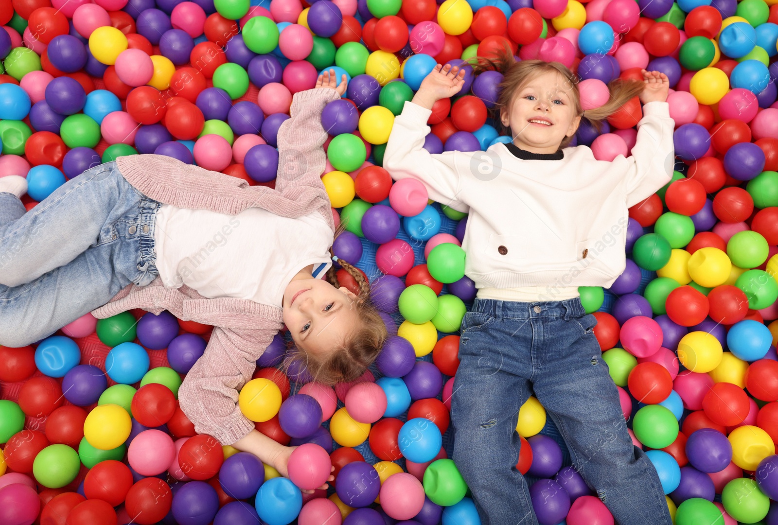 Photo of Happy little kids lying on many colorful balls, top view