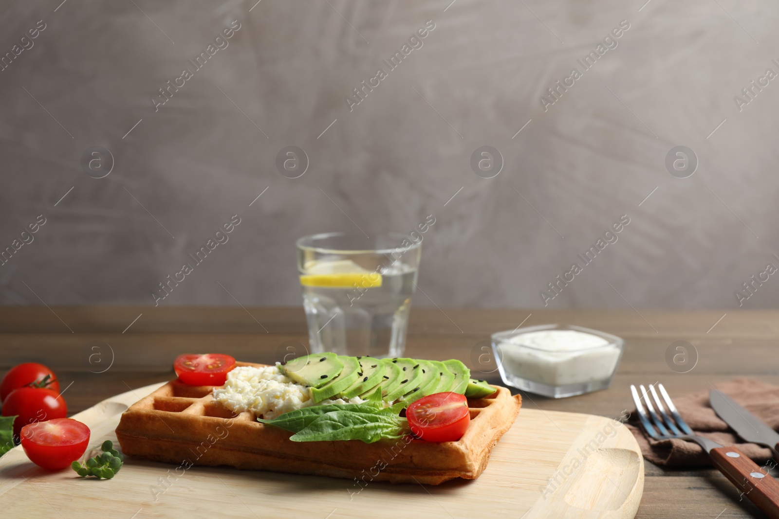 Photo of Fresh Belgian waffle with avocado, tomatoes and basil served for breakfast on wooden table