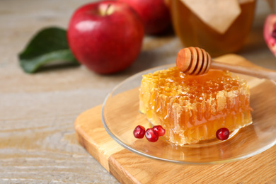 Photo of Honeycomb with pomegranate seeds near apples on wooden table, closeup. Rosh Hashanah holiday