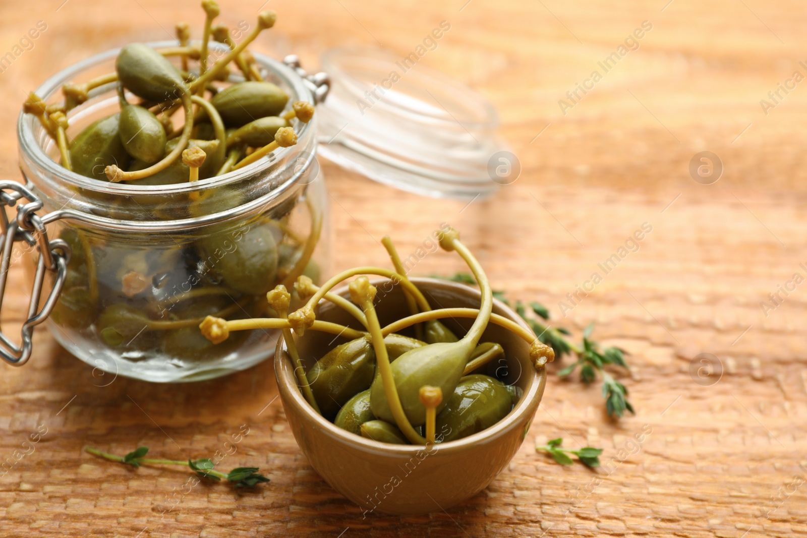 Photo of Delicious pickled capers and thyme twigs on wooden table, closeup