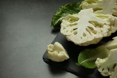 Photo of Cut fresh raw cauliflowers on black table. Space for text