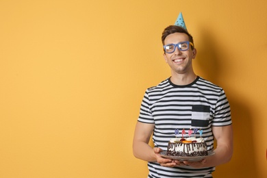 Photo of Young man with birthday cake on color background