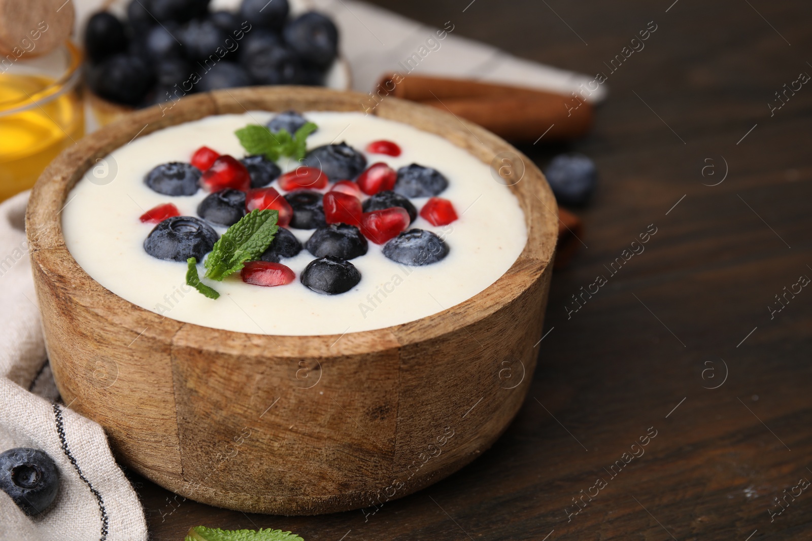 Photo of Bowl of delicious semolina pudding with blueberries, pomegranate and mint on wooden table, closeup. Space for text