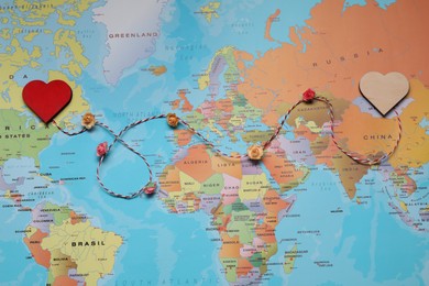 Photo of Decorative cord with hearts on world map symbolizing connection in long-distance relationship, top view
