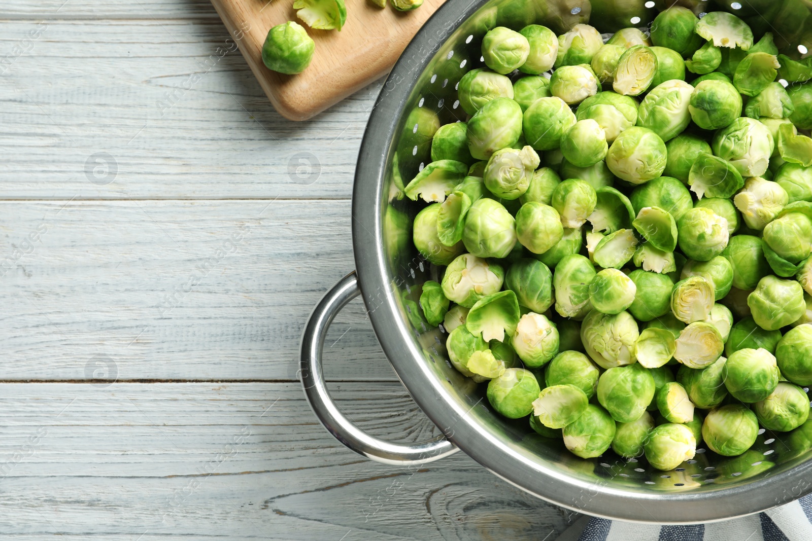 Photo of Colander with Brussels sprouts on wooden background, top view. Space for text