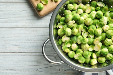 Photo of Colander with Brussels sprouts on wooden background, top view. Space for text