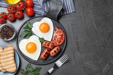 Delicious breakfast with heart shaped fried eggs and  sausages served on dark grey table, flat lay. Space for text