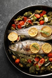 Baked fish with vegetables, rosemary and lemon on black textured table, top view