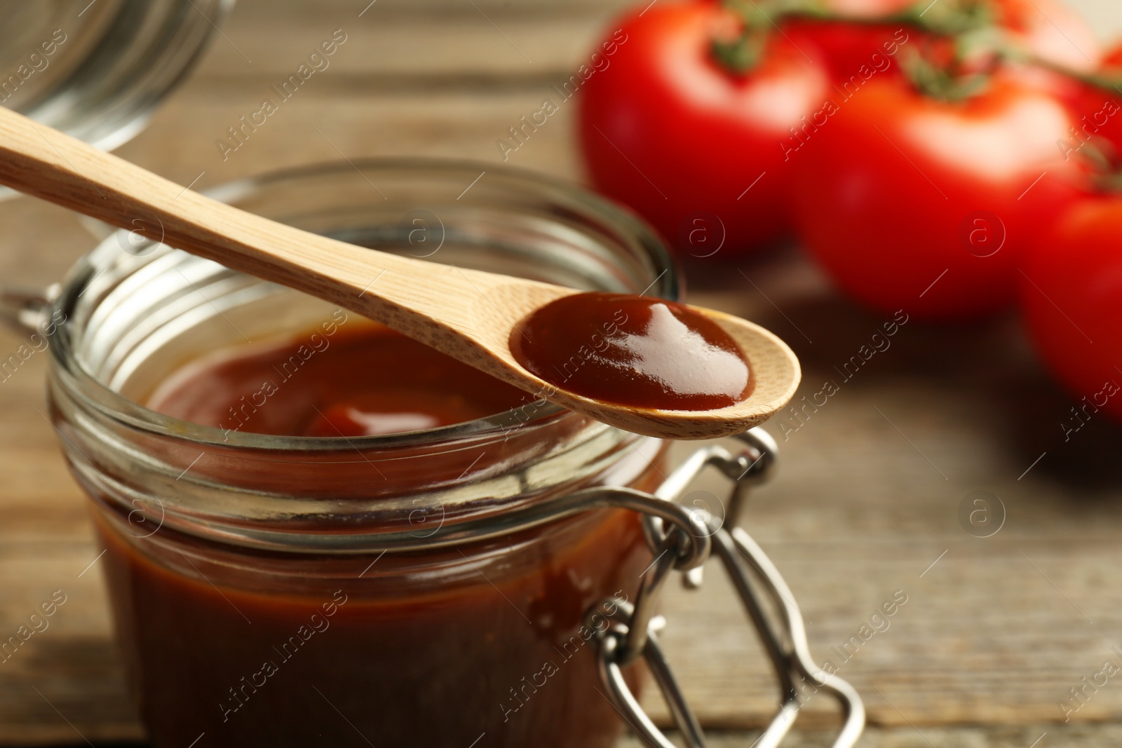 Photo of Tasty barbeque sauce in jar and spoon on table, closeup