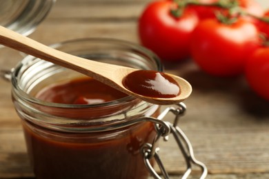 Photo of Tasty barbeque sauce in jar and spoon on table, closeup
