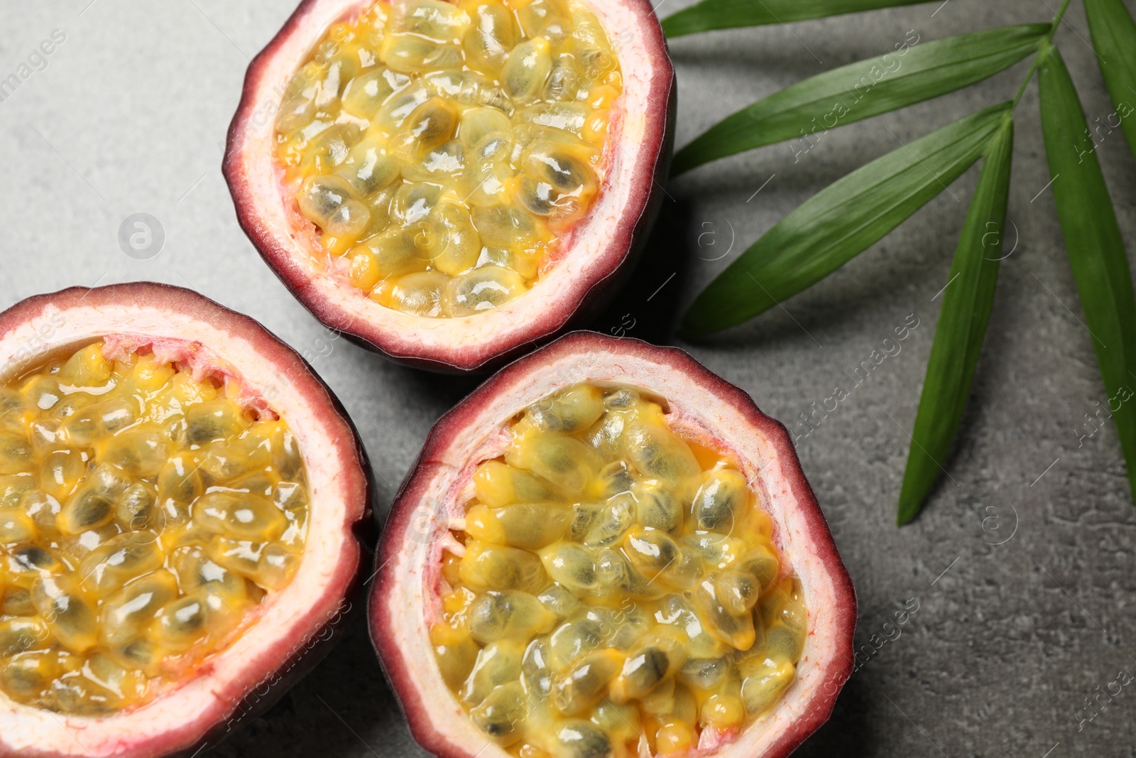 Photo of Halves of passion fruits (maracuyas) and palm leaf on grey table, flat lay