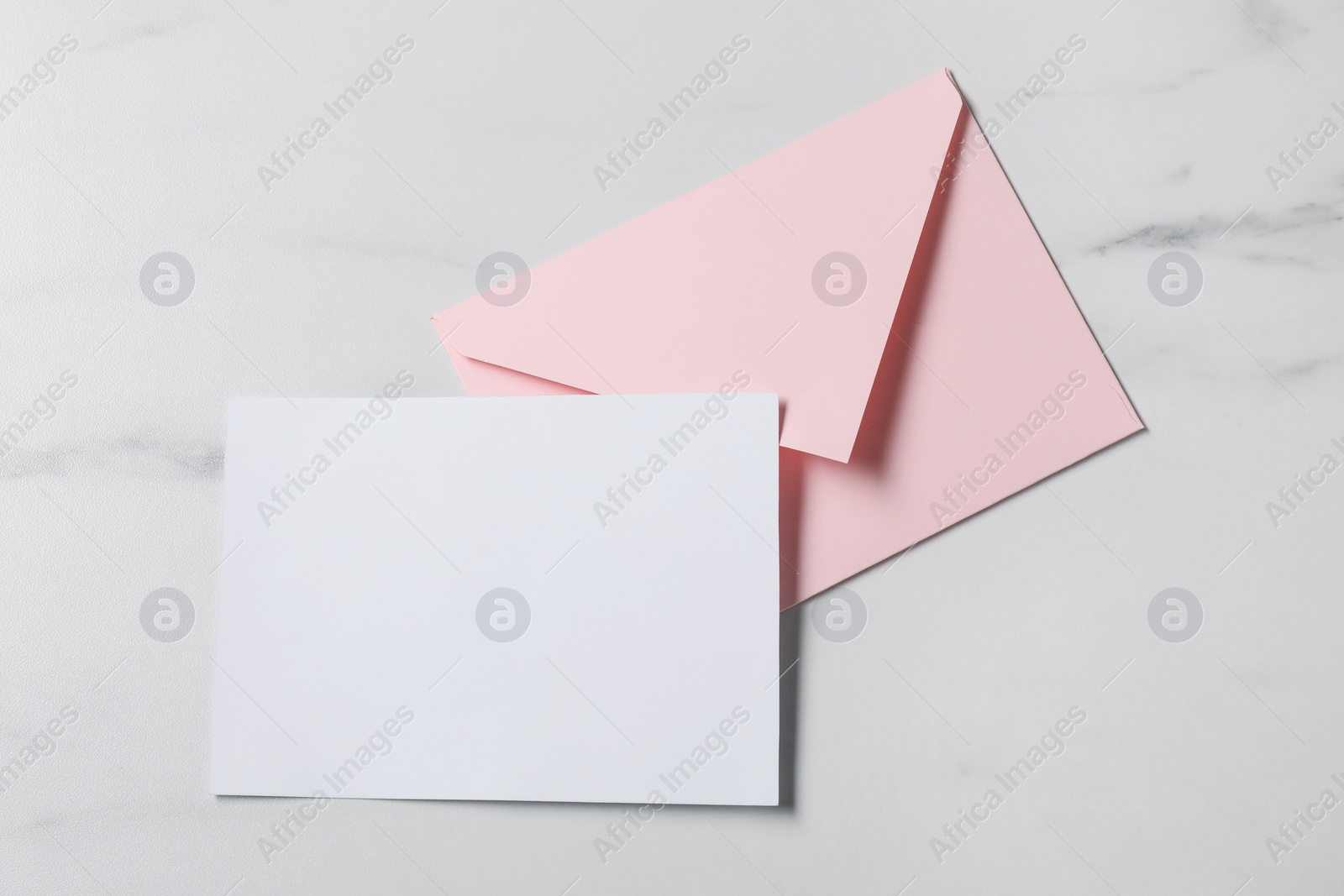 Photo of Blank sheet of paper and letter envelope on white marble table, top view