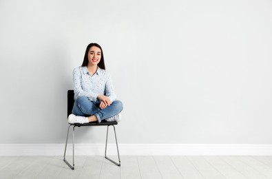 Photo of Young woman sitting on chair near white wall in office, space for text