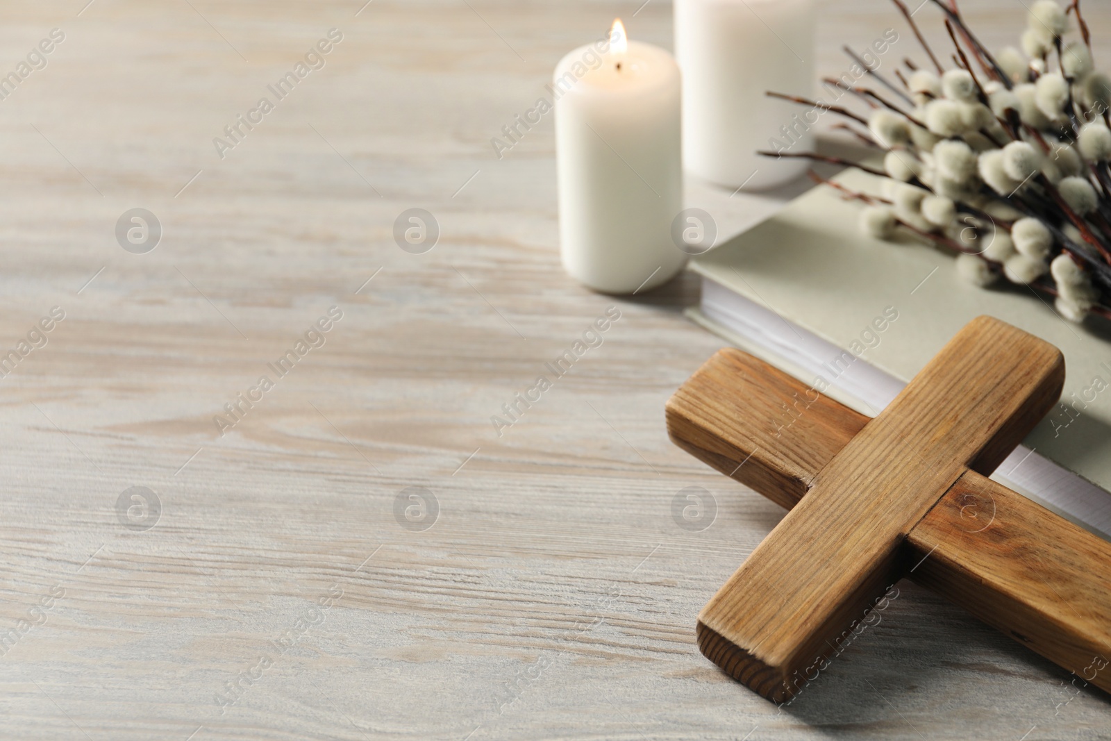 Photo of Burning candles, cross, book and willow branches on wooden table. Space for text