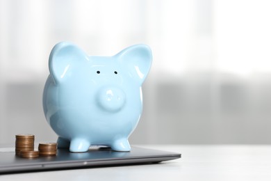 Photo of Piggy bank, stacked coins and laptop on white table indoors. Space for text