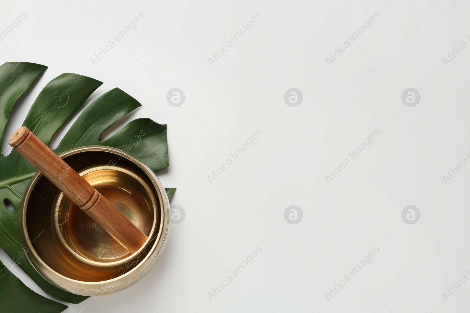 Photo of Golden singing bowls, mallet and monstera leaf on white background, flat lay. Space for text