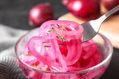 Fork with tasty pickled onion slices over jar on table, closeup