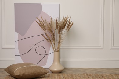 Fluffy reed plumes and painting near white wall indoors, space for text. Interior elements