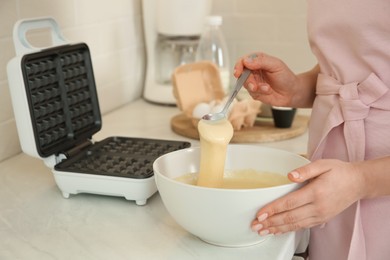 Photo of Woman preparing dough near Belgian waffle maker in kitchen, closeup