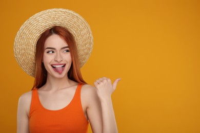 Photo of Happy woman showing her tongue and pointing at something on orange background. Space for text
